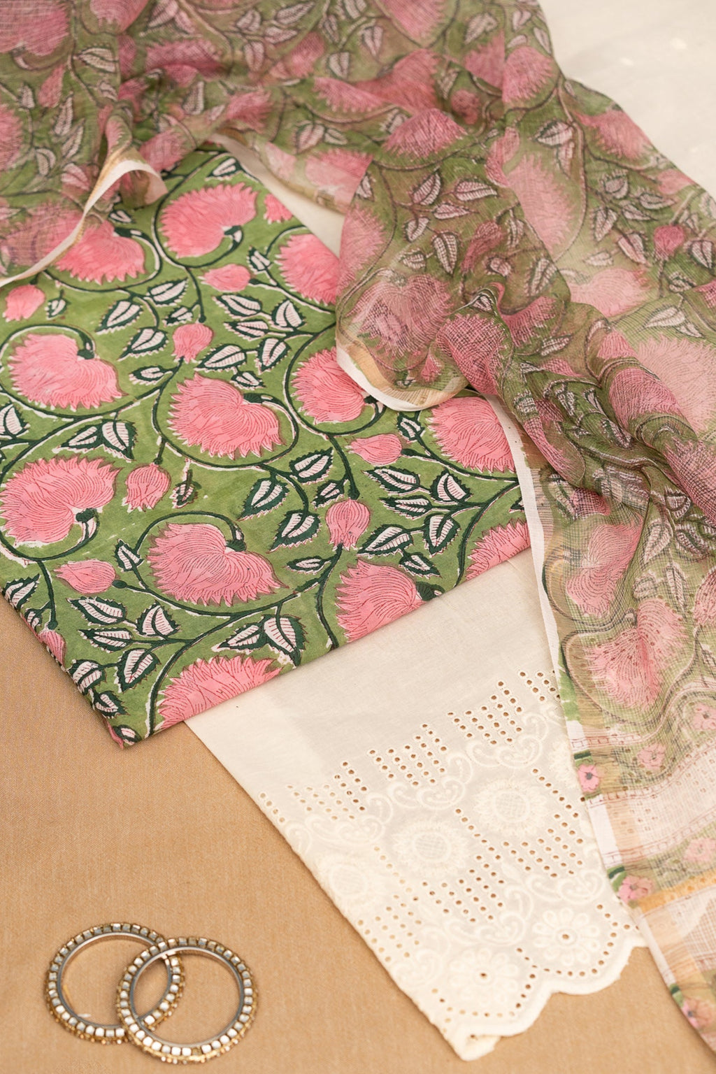 Fabric with pink and green floral pattern on a beige surface with lace and rings.